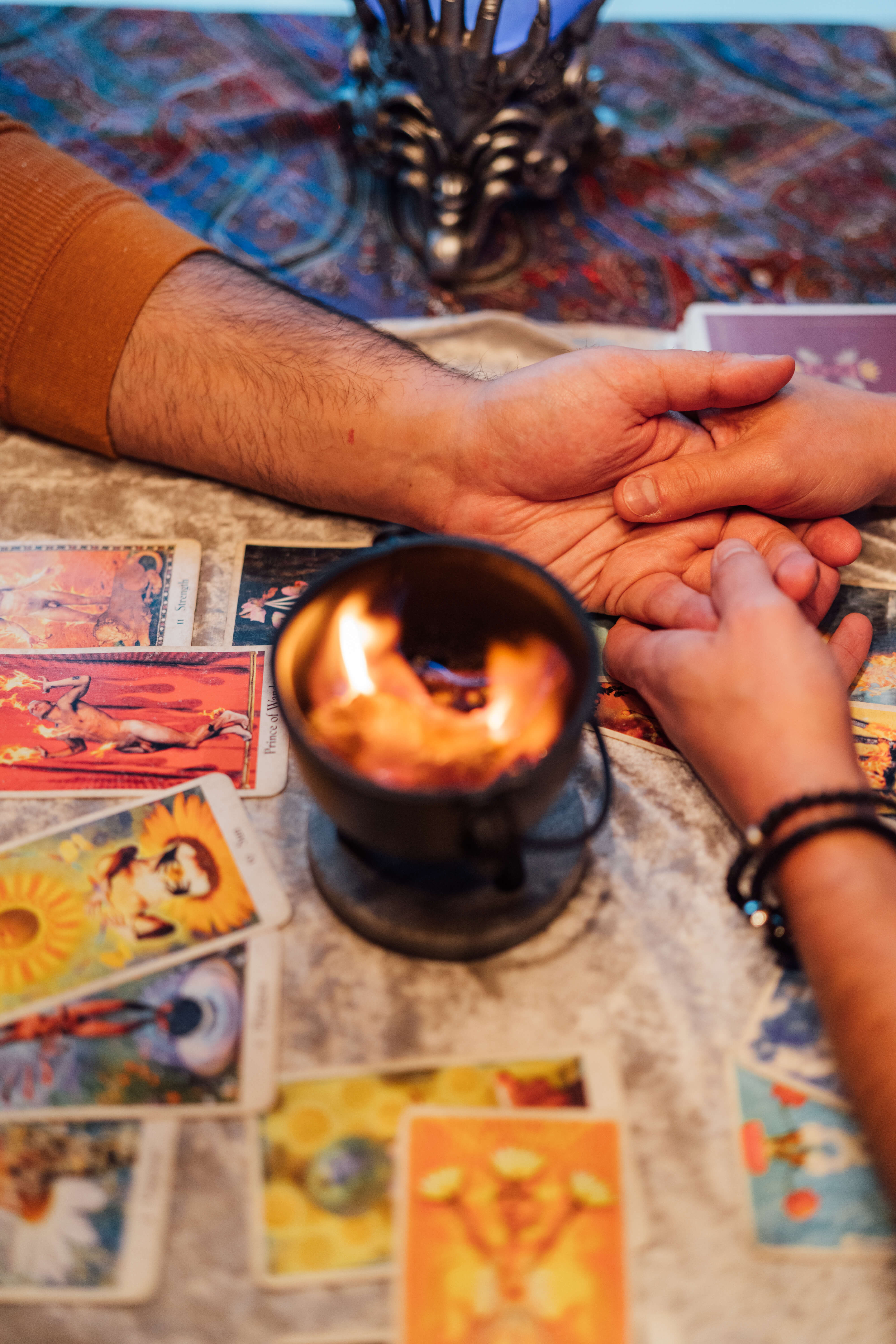 Two hands meeting over a candle and tarot cards